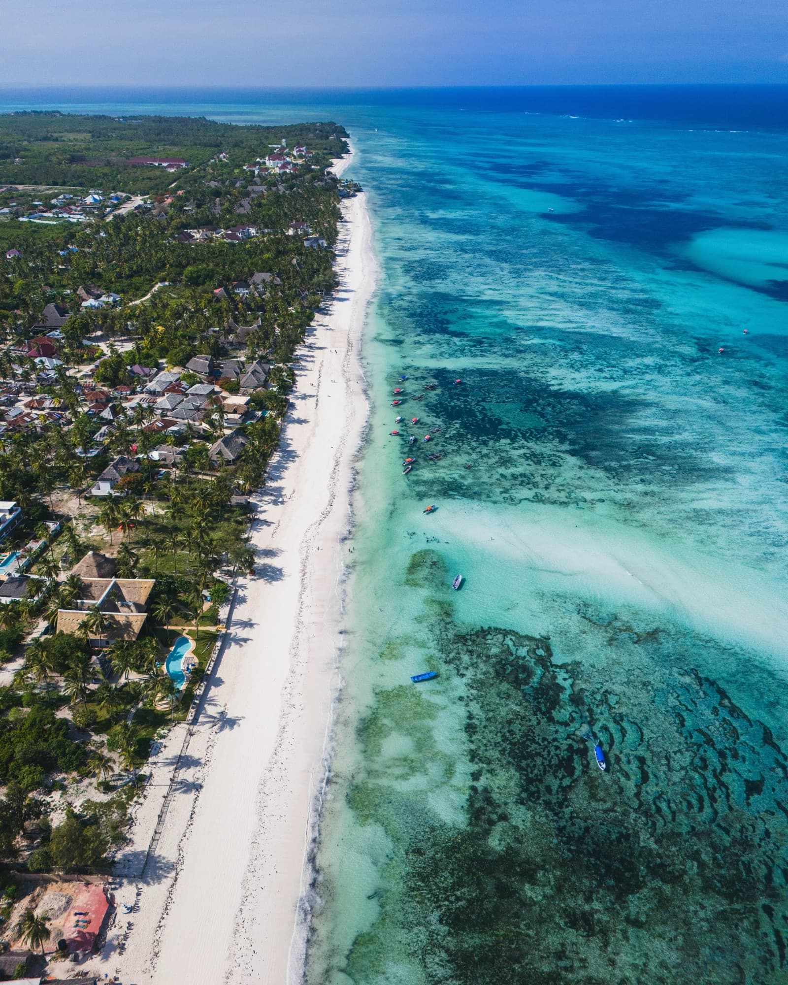 Aerial view of the Zanzibar coastline: beachfront villas and resorts along white sand, reef visible offshore